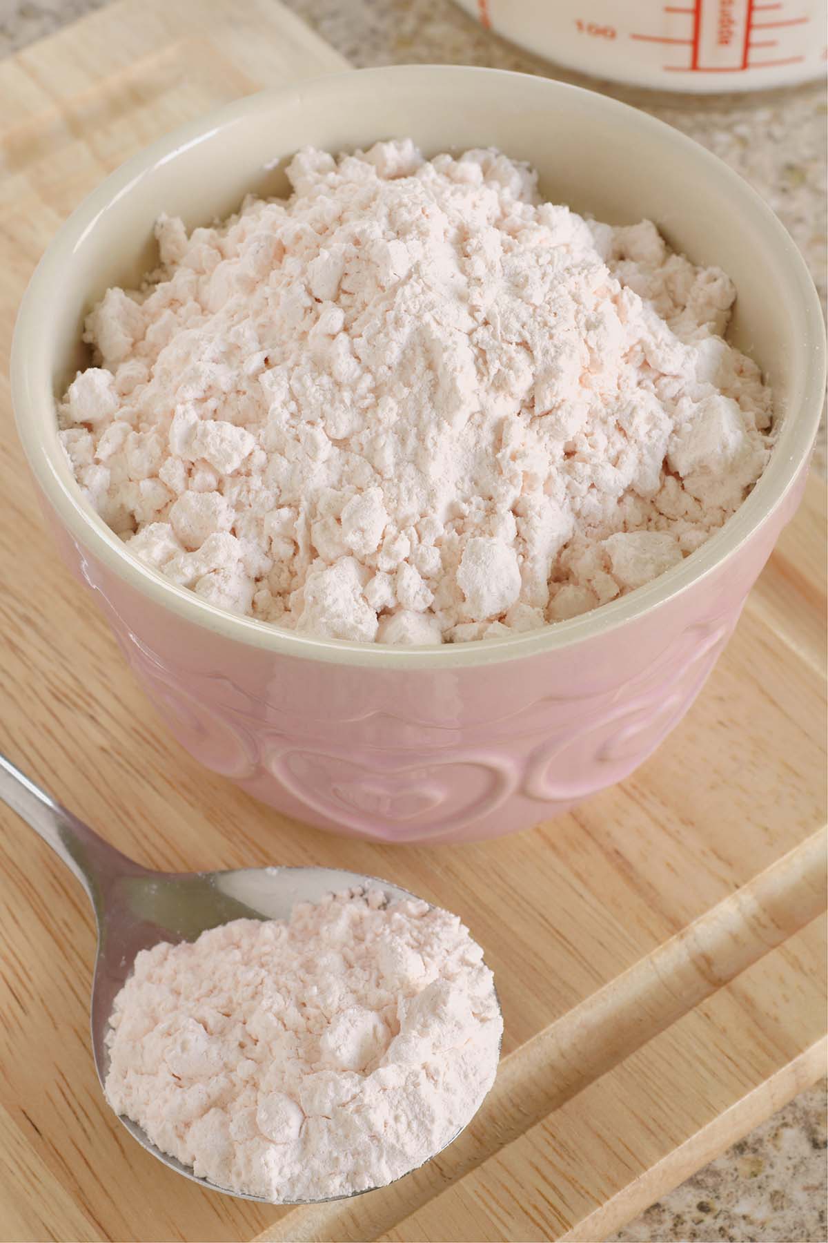 Custard powder in a pink bowl and on a spoon.