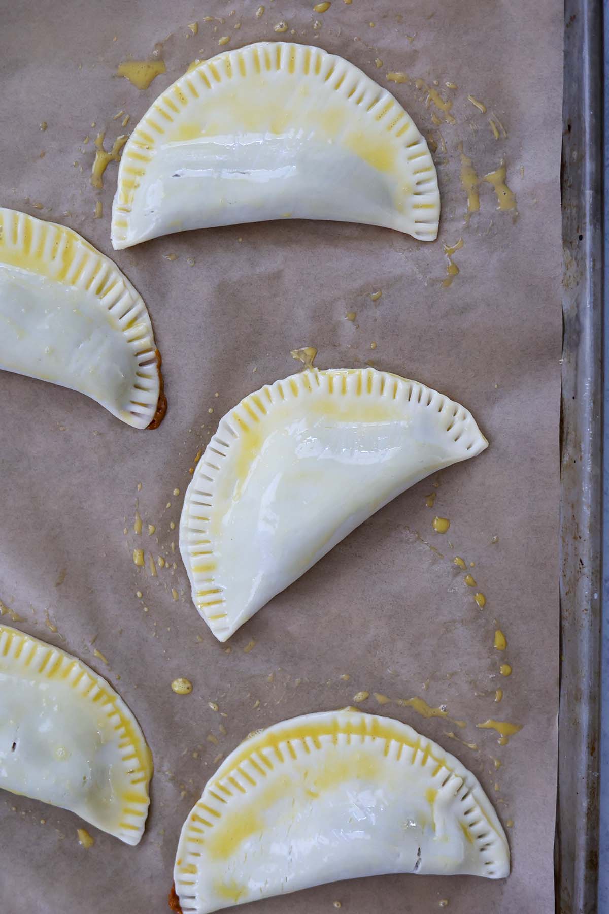 empanadas on a baking sheet brushed with egg wash.