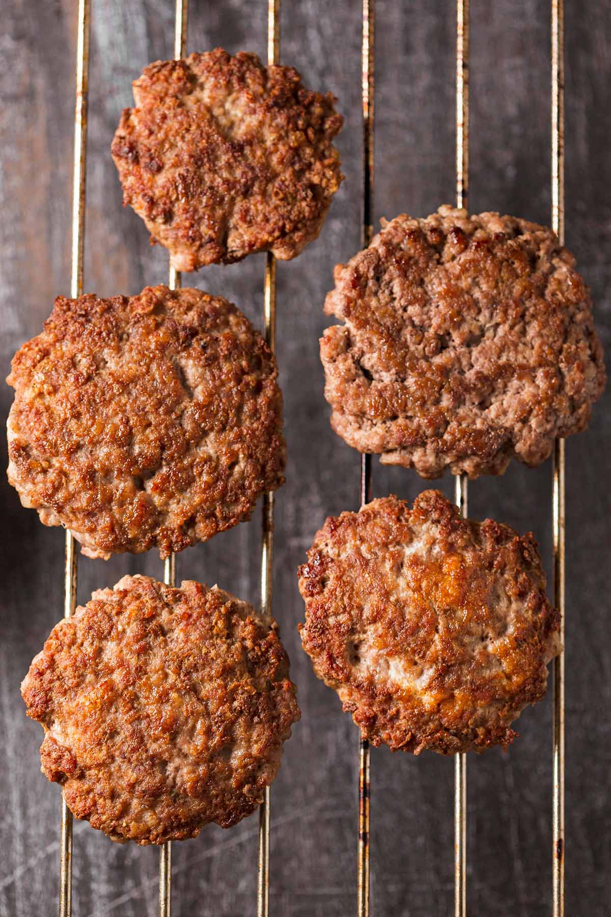 Five cooked beef patties on a wire rack.