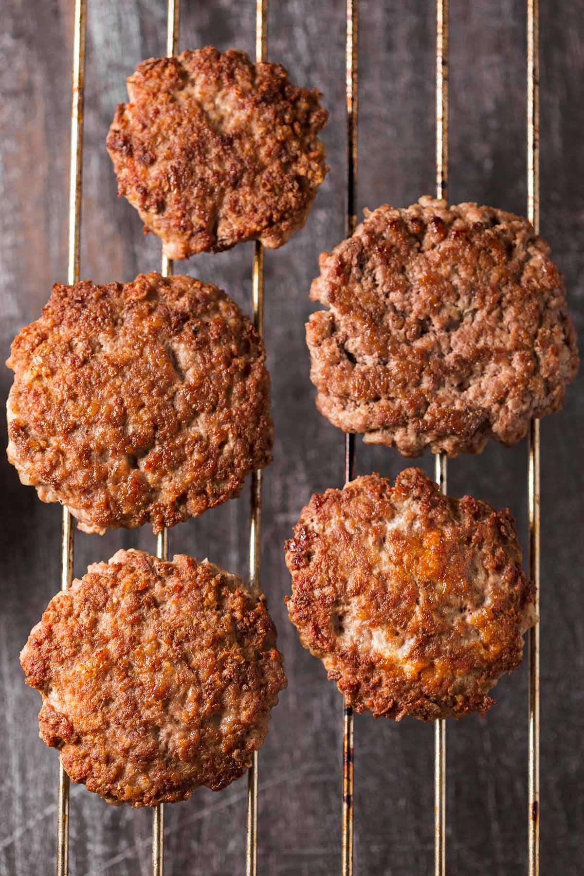 Five cooked beef patties on a wire rack. 