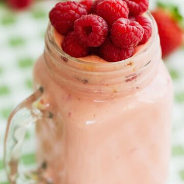 raspberry milkshake in a glass with fresh raspberries on top.