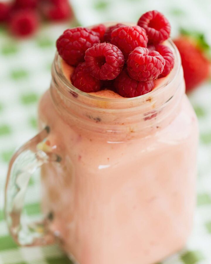raspberry milkshake in a glass with fresh raspberries on top.