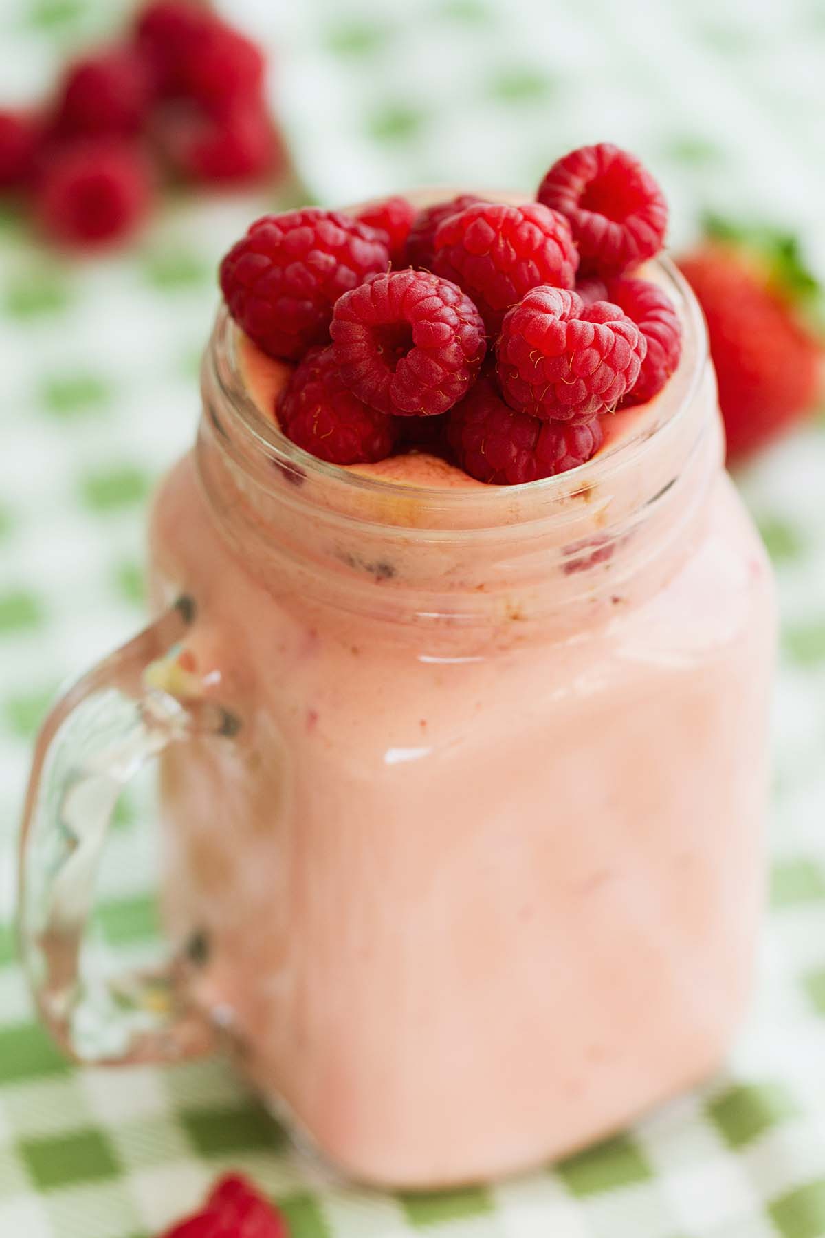 raspberry milkshake in a glass with fresh raspberries on top. 