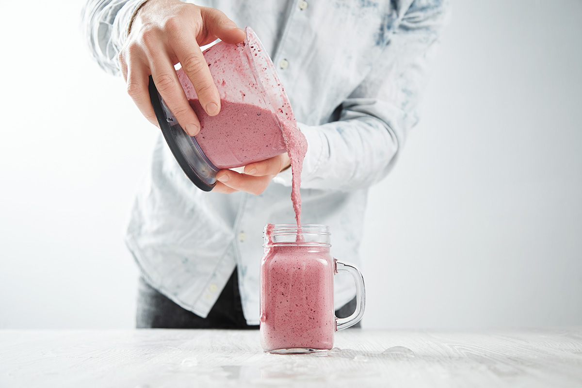 person pouring raspberry milkshake from a blender into a glass.