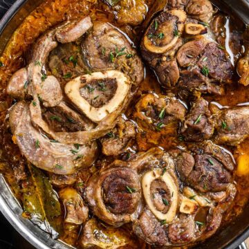 beef shank stew in a skillet with a dark towel on the side.