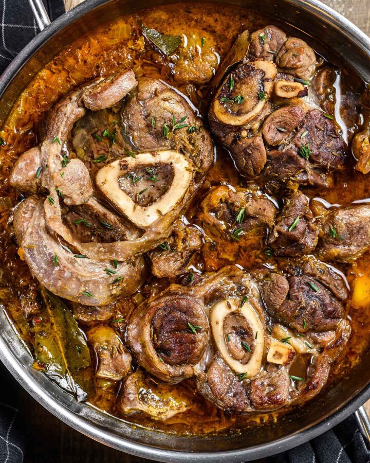 beef shank stew in a skillet with a dark towel on the side.