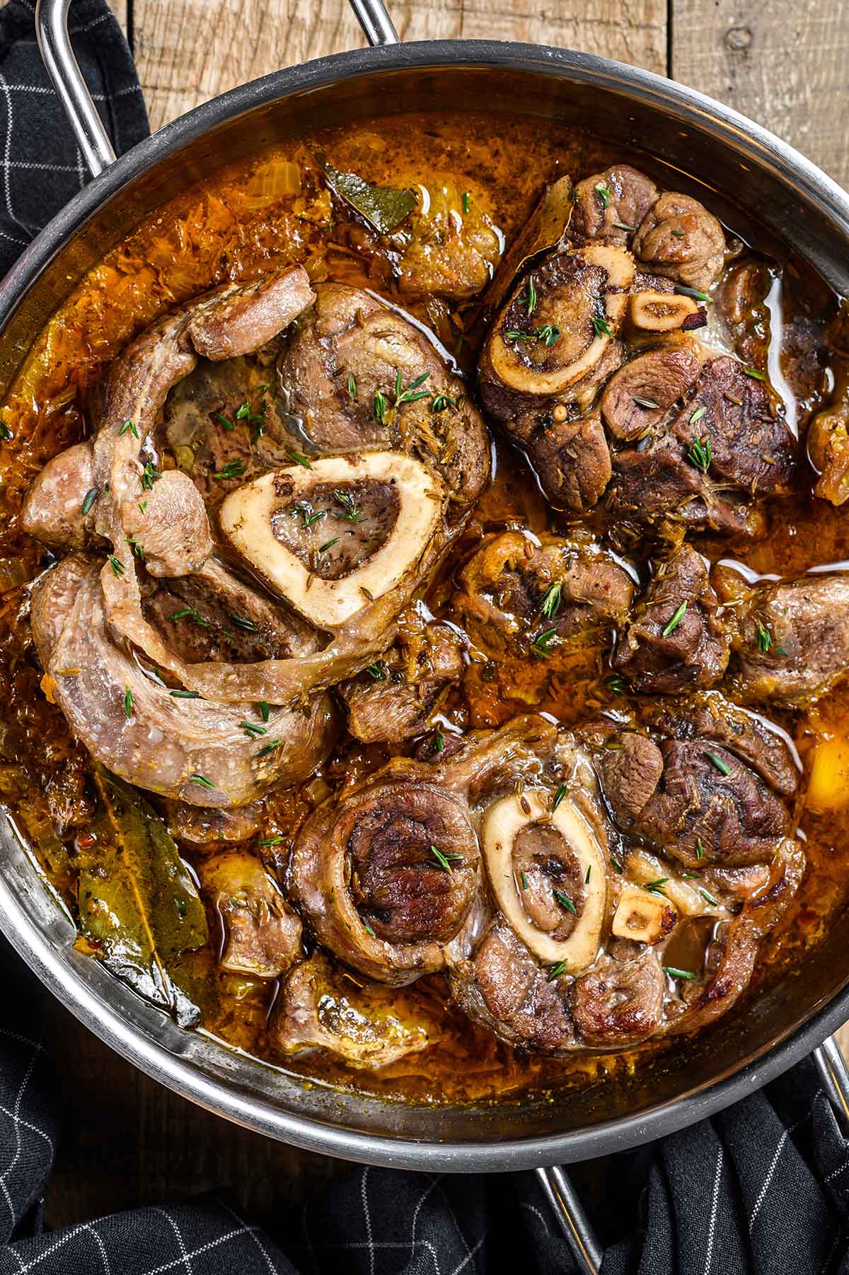 beef shank stew in a skillet with a dark towel on the side. 