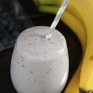 blueberry banana protein smoothie with a straw.