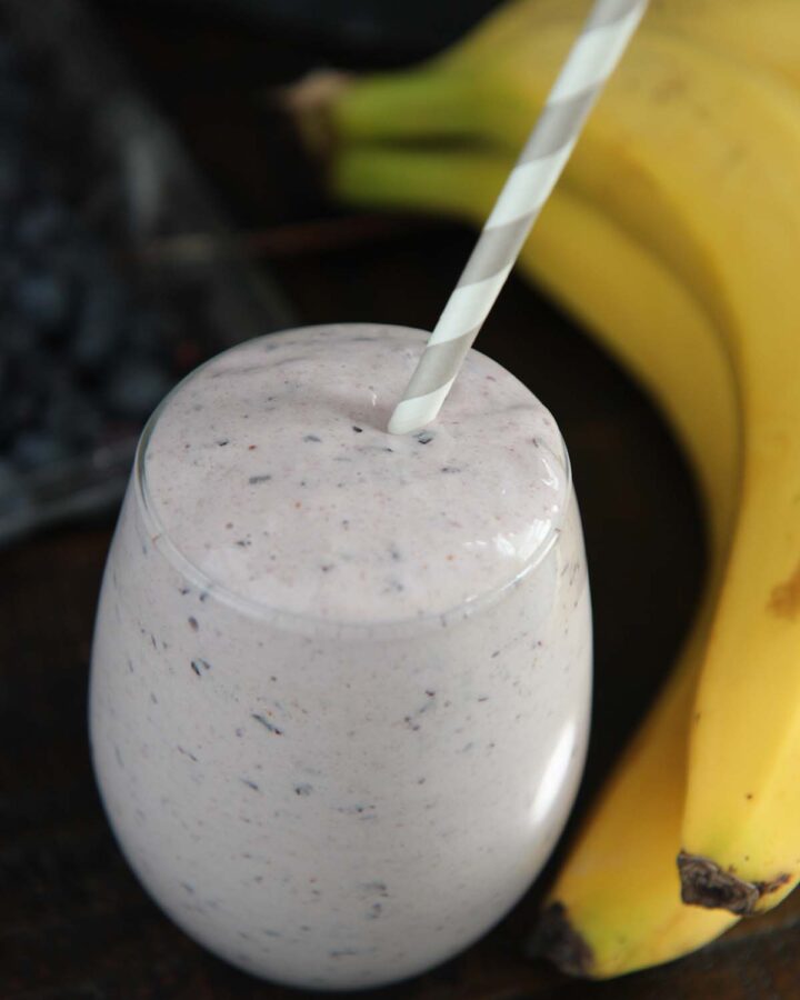 blueberry banana protein smoothie with a straw.