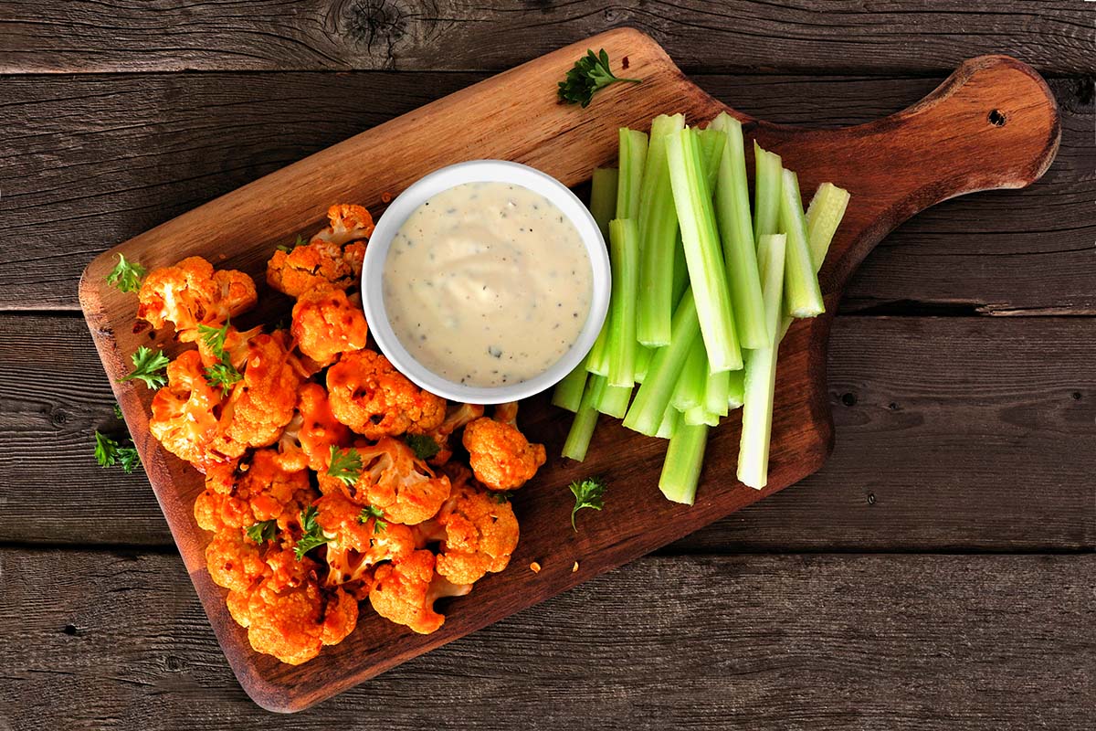 buffalo cauliflower with blue cheese dip and celery sticks on the side.