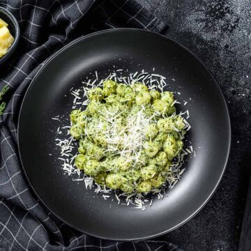 creamy pesto gnocchi on a plate with a fork and knife on the side.