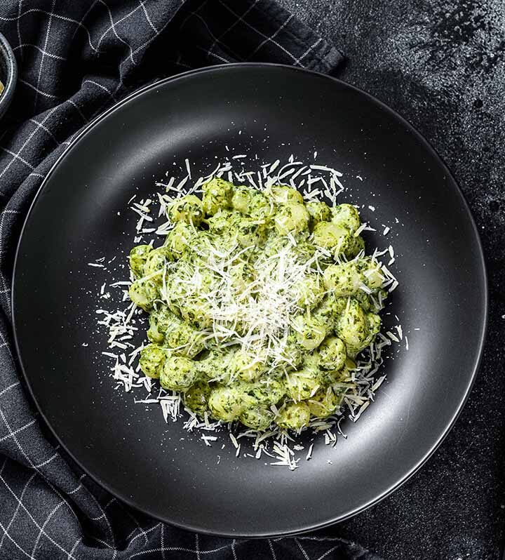 creamy pesto gnocchi on a plate with a fork and knife on the side.