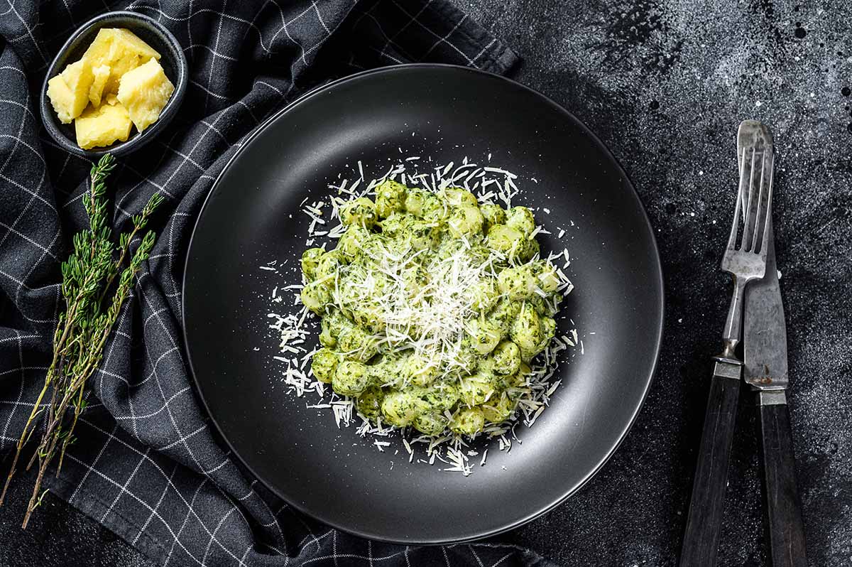 creamy pesto gnocchi on a plate with a fork and knife on the side.