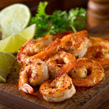 old bay shrimp with lime wedges on a wooden board.