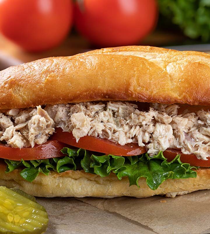 albacore tuna salad sandwich with pickles and chips on the side.