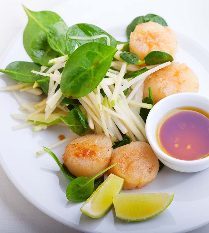 cooked bay scallops on a white plate with a lime wedge and sauce on the side.