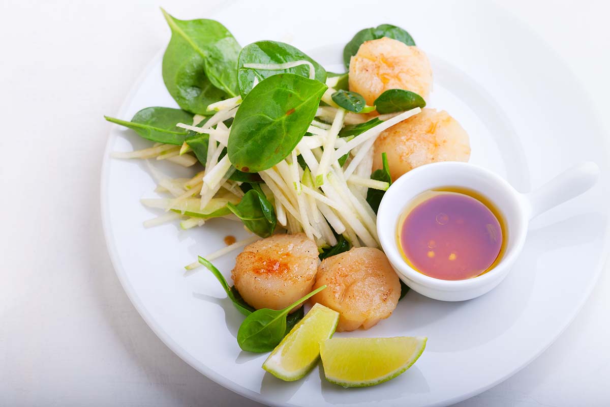 cooked bay scallops on a white plate with a lime wedge and sauce on the side. 