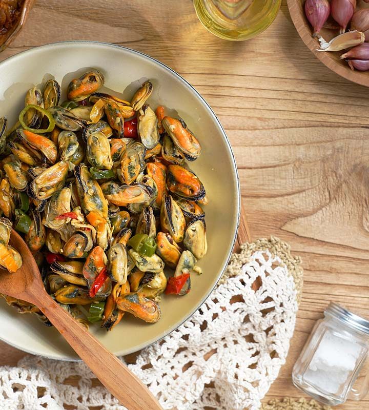 sauteed canned oysters on a white plate with a wooden spoon.