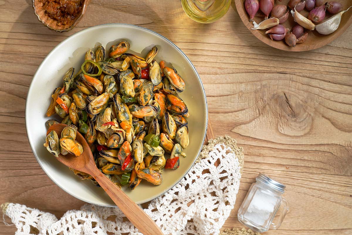 sauteed canned oysters on a white plate with a wooden spoon.