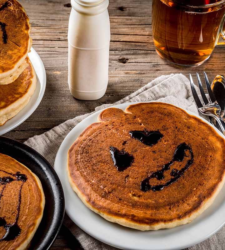 Halloween pancakes with tea, milk, and utensils on the side.