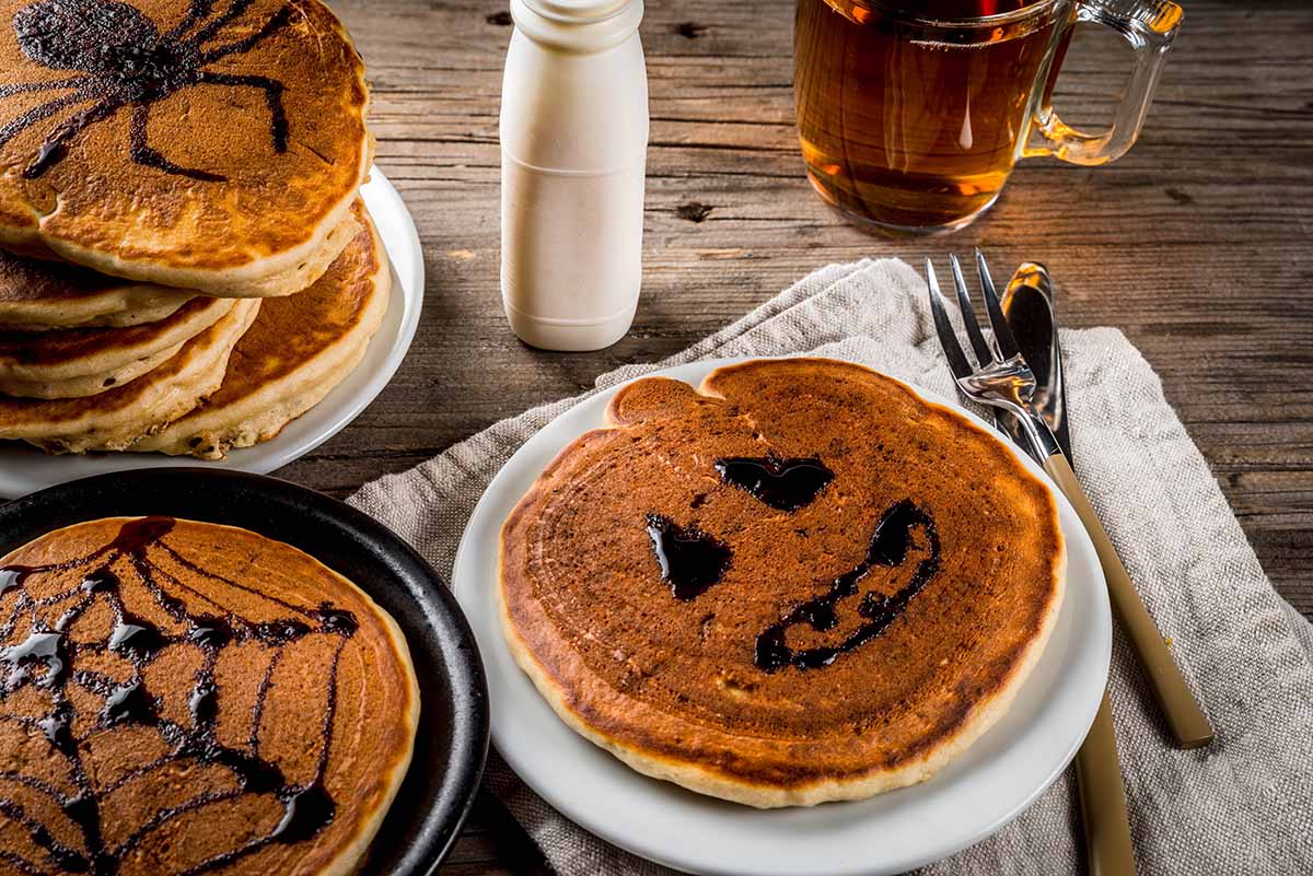 Halloween pancakes with tea, milk, and utensils on the side.