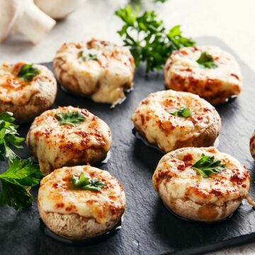 eight stuffed mushrooms on a black plate.