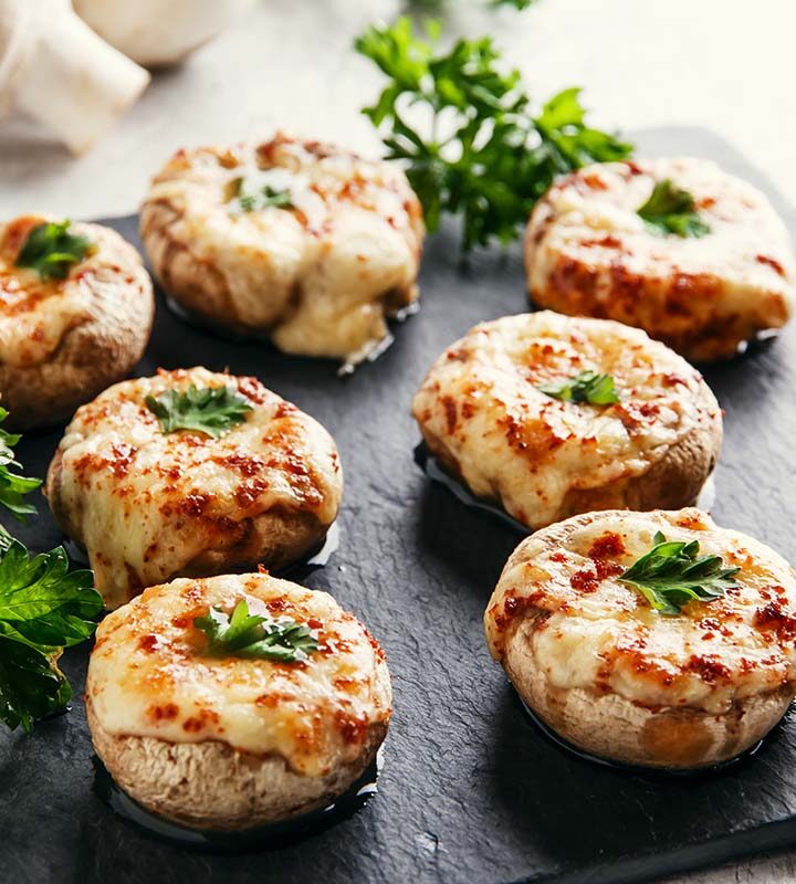 eight stuffed mushrooms on a black plate.