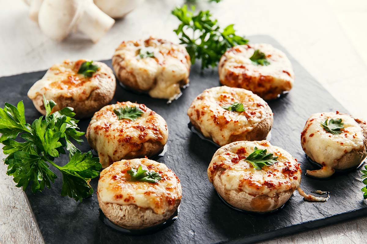 eight stuffed mushrooms on a black plate.