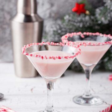 two white chocolate peppermint martinis with a tumbler in the background.