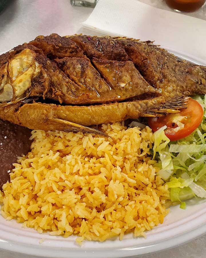 fried whole tilapia fish with yellow rice, beans, and salad.