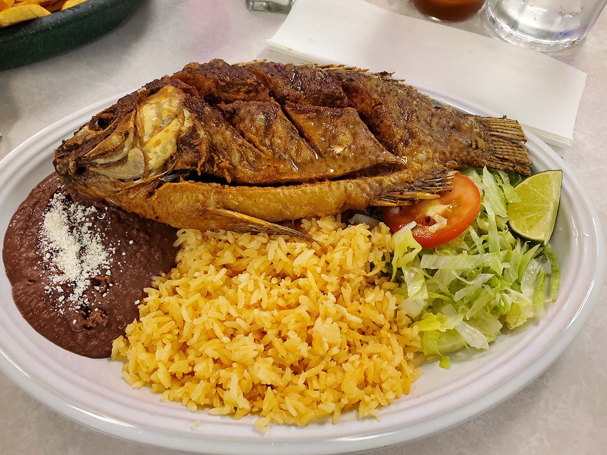 fried whole tilapia fish with yellow rice, beans, and salad.