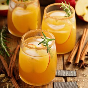 three apple cider cocktails on a wooden board.