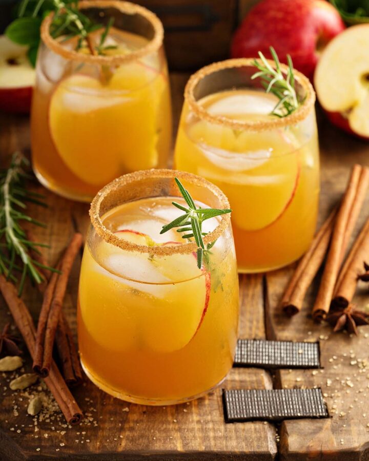 three apple cider cocktails on a wooden board.