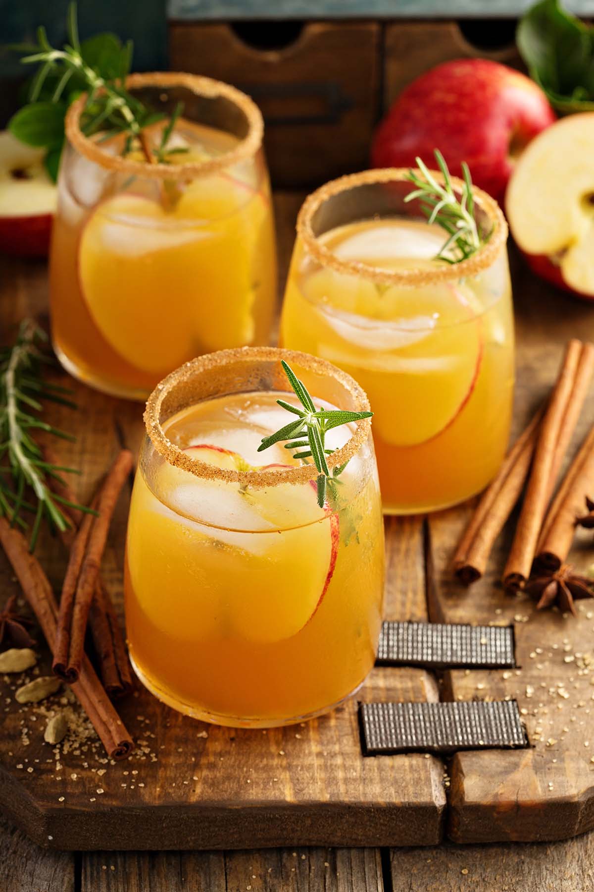 three apple cider cocktails on a wooden board. 