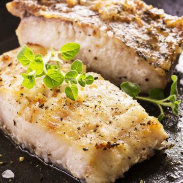 Two cooked grouper fish fillets in a cast iron skillet.
