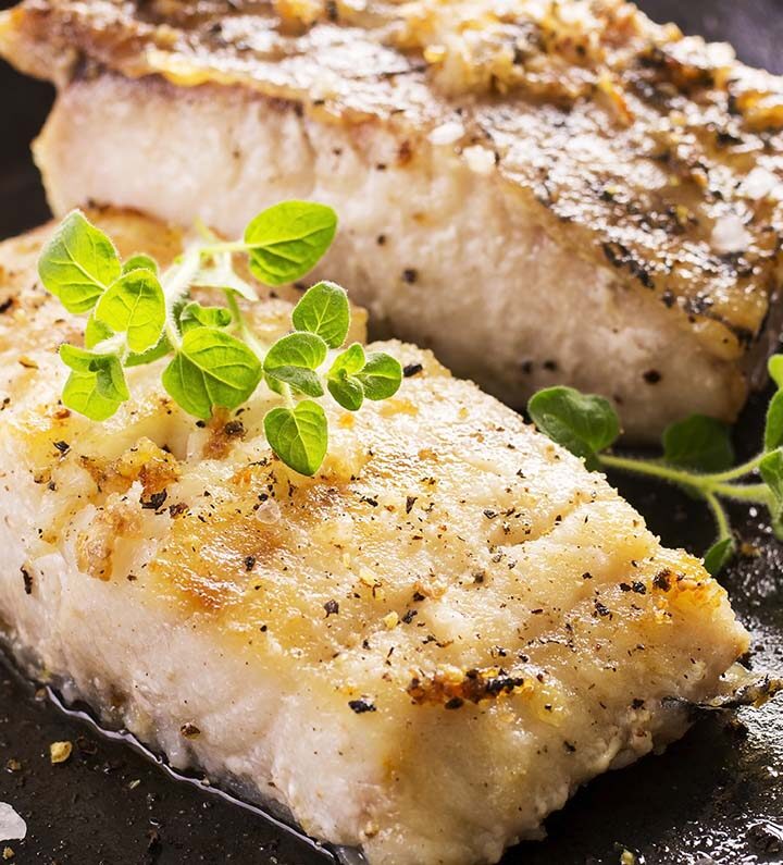 Two cooked grouper fish fillets in a cast iron skillet.