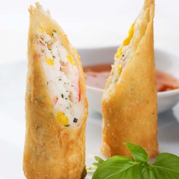 fried lobster spring rolls with sauce and basil leaves on the side.