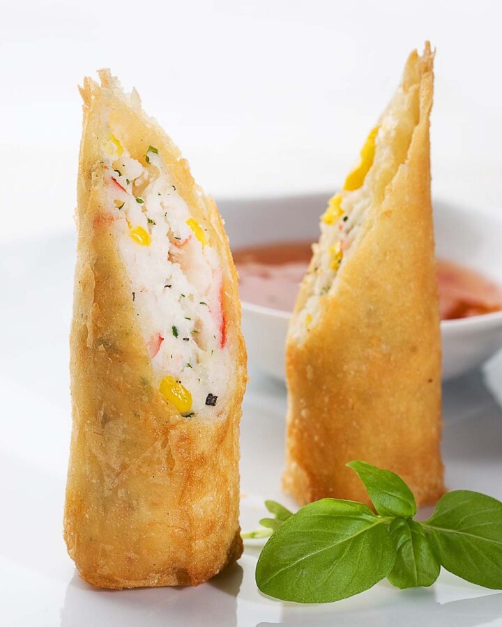 fried lobster spring rolls with sauce and basil leaves on the side.