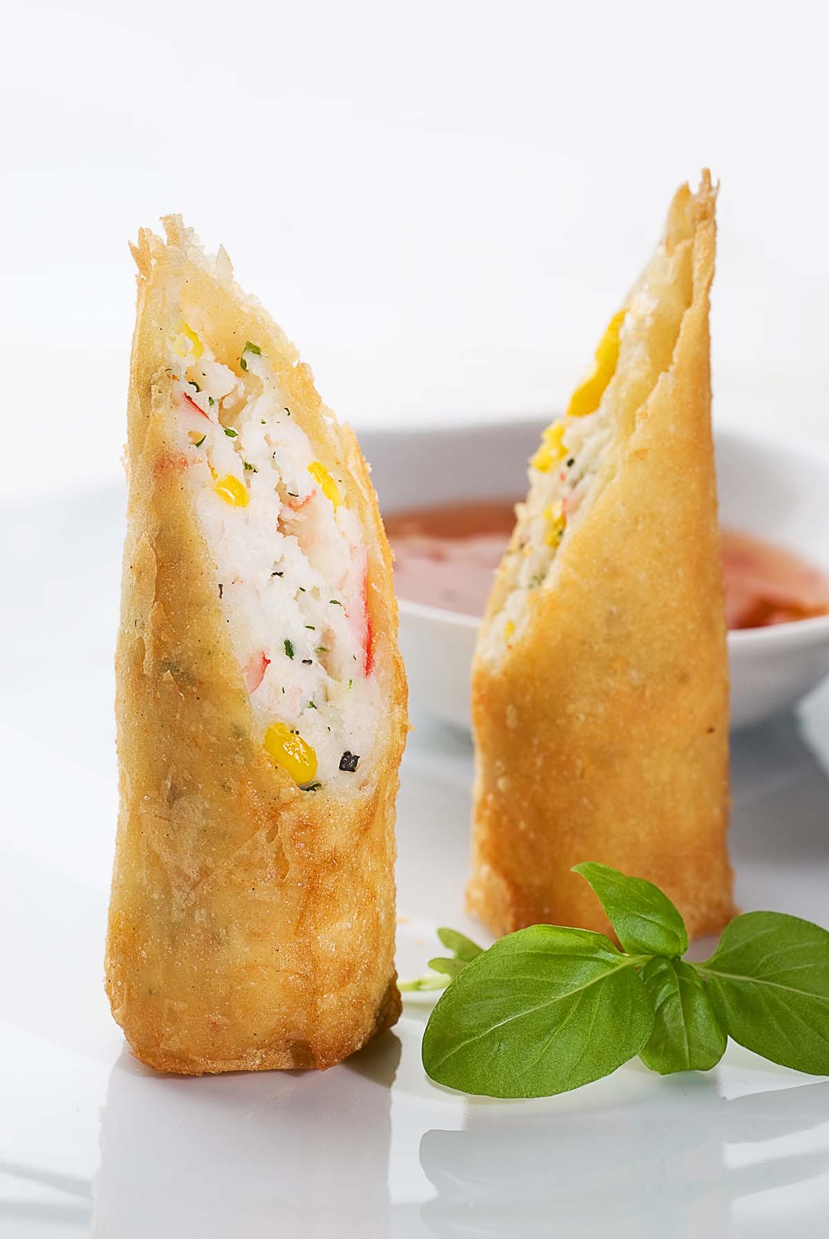 fried lobster spring rolls with sauce and basil leaves on the side.