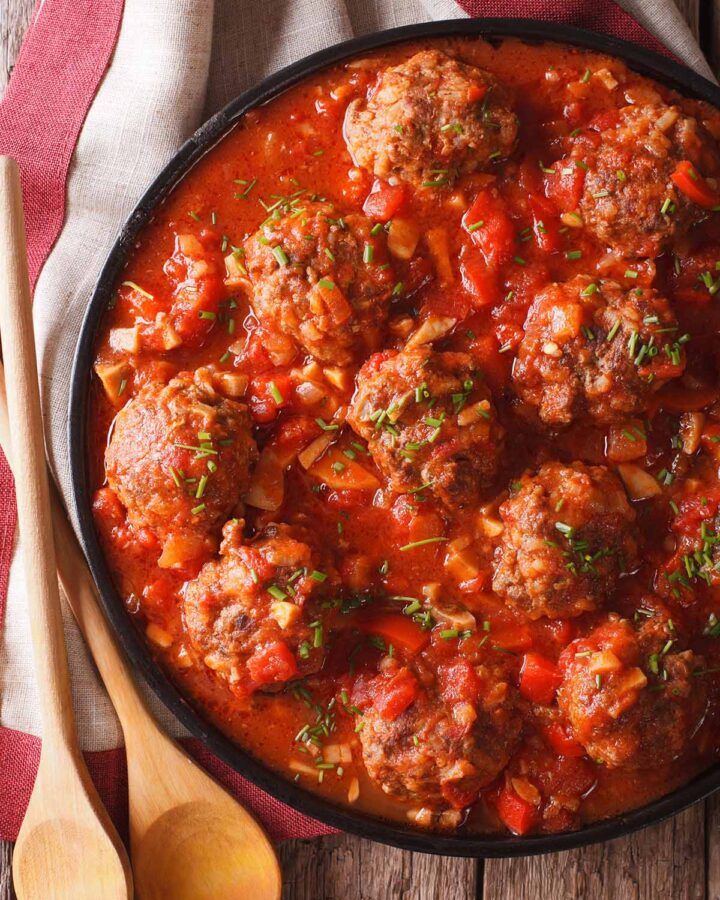 cooked meatballs in marinara sauce with wooden spoons on the side.