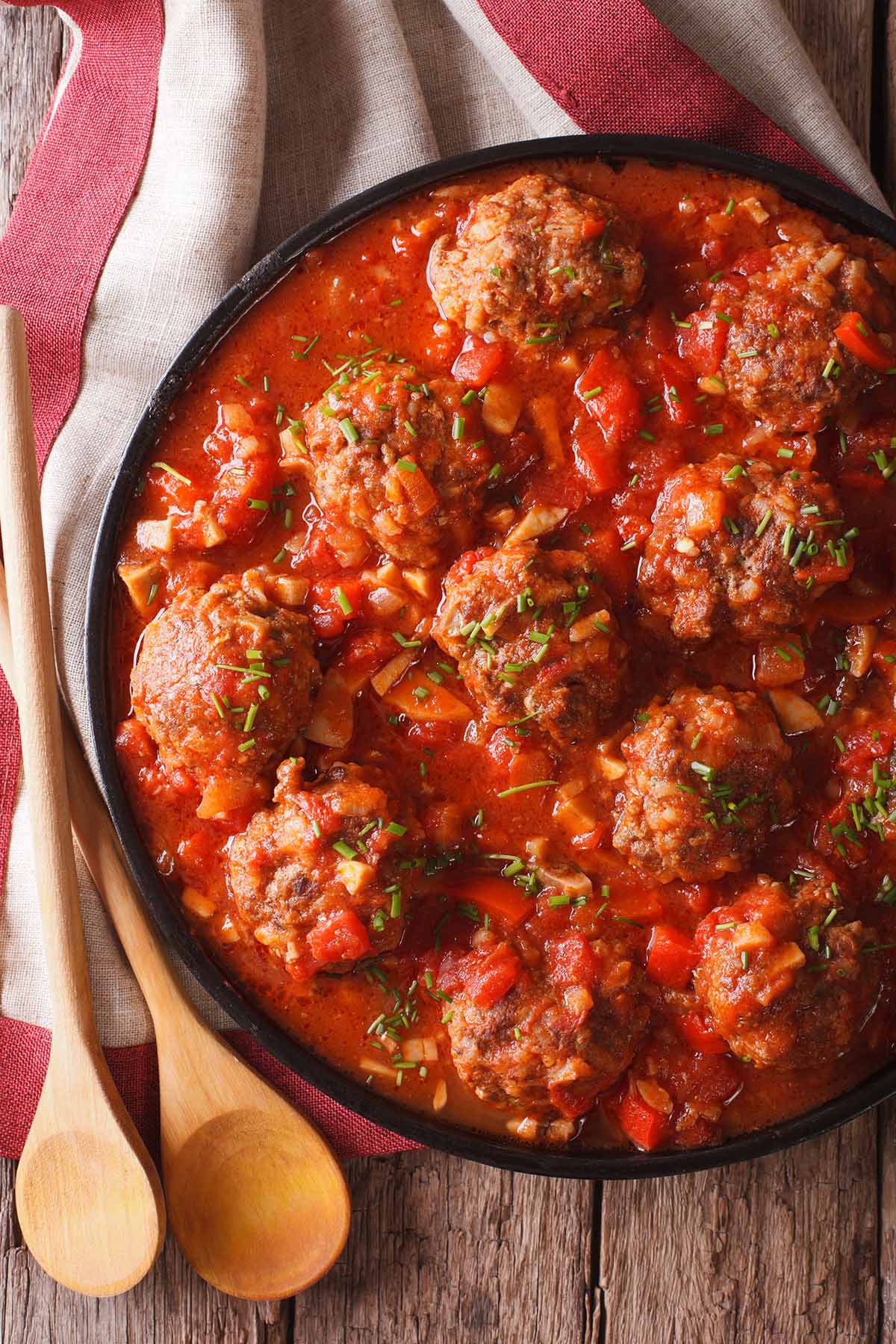 cooked meatballs in marinara sauce with wooden spoons on the side. 