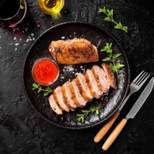 sliced smoked breast on a black plate with a fork and knife on the side.