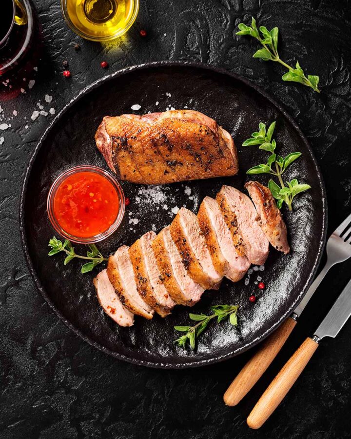 sliced smoked breast on a black plate with a fork and knife on the side.