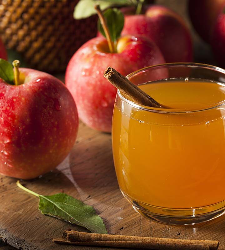 apple cider in a glass with red apples in the background.