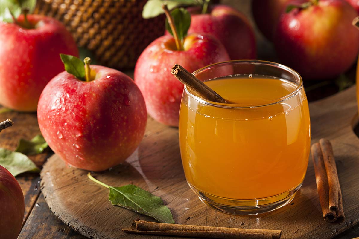 apple cider in a glass with red apples in the background.