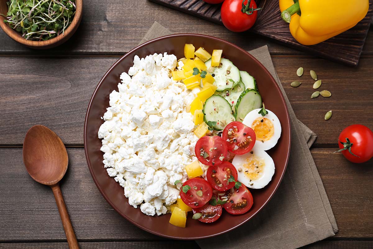 cottage cheese in a bowl with tomatoes, eggs, peppers, and cucumbers.