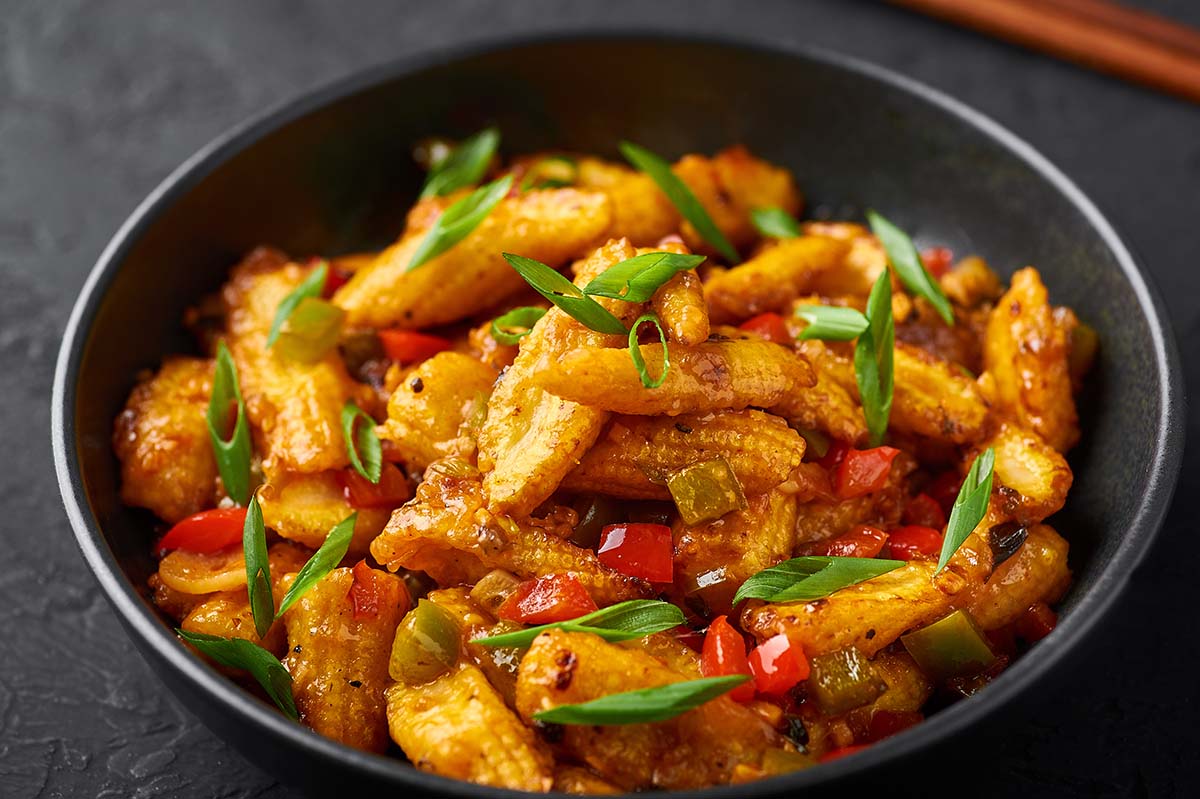 baby corn in a bowl with scallions and peppers.