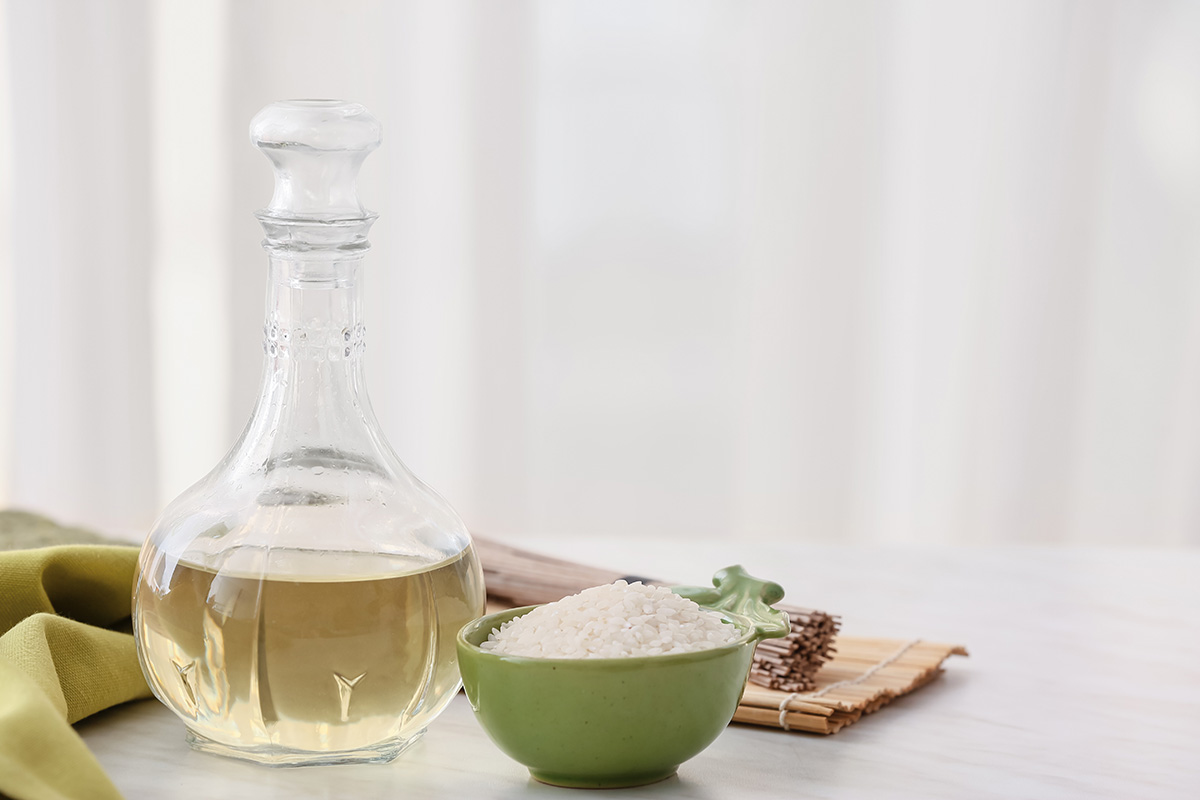 Rice vinegar in a glass bottle with a bowl of white rice on the side.
