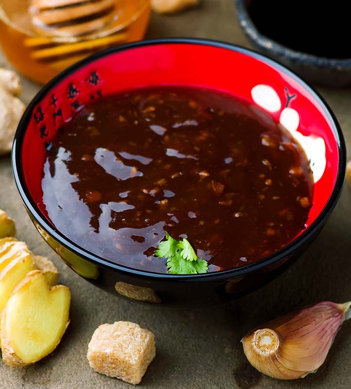 Teriyaki sauce in a red bowl with ginger and garlic on the side.
