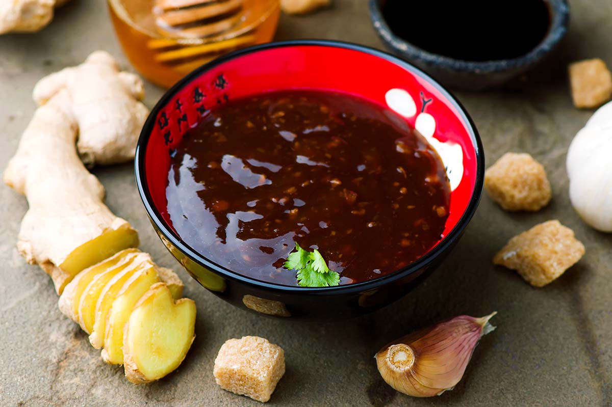 Teriyaki sauce in a red bowl with ginger and garlic on the side. 